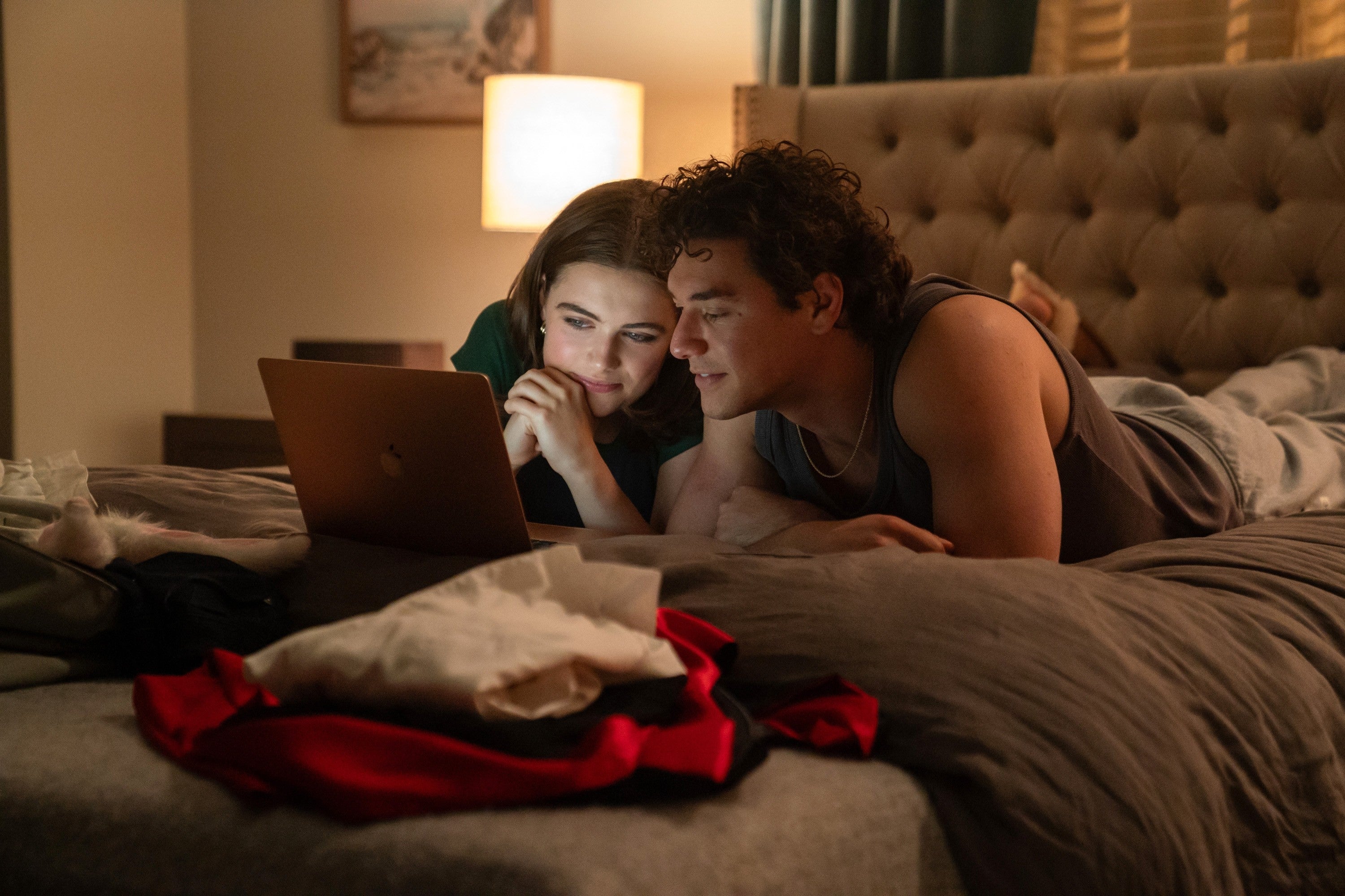 Two people lie on a bed, intently watching a laptop screen