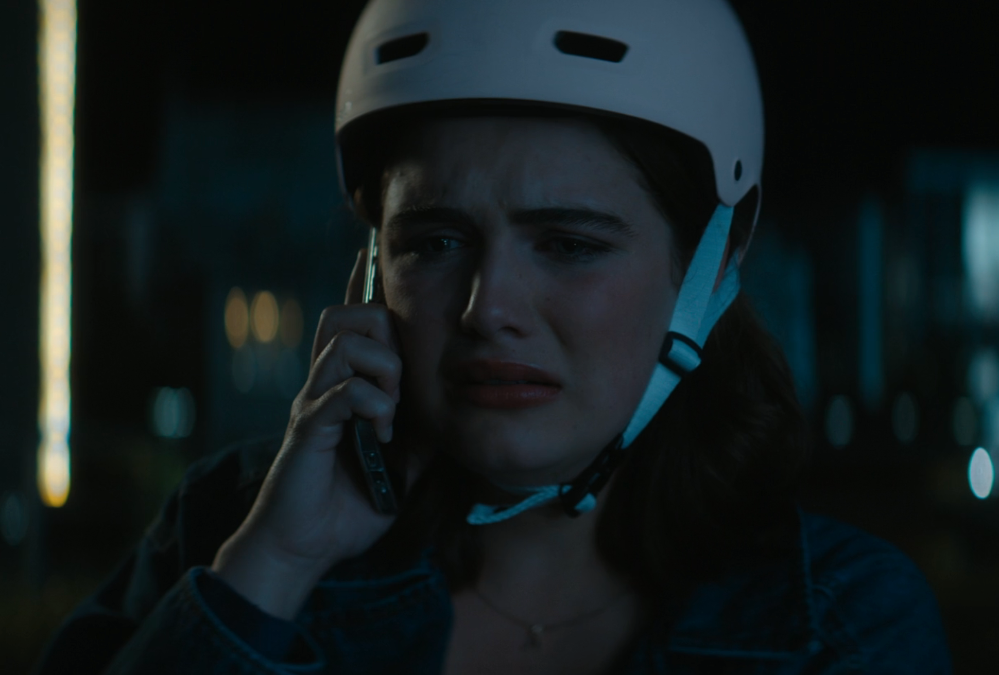 A person wearing a helmet is talking on a phone with a concerned expression, suggesting a tense or emotional moment