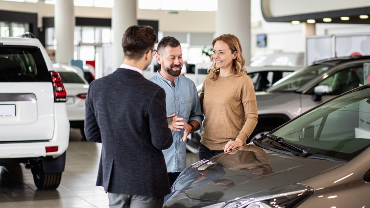 Mladi prodavač automobila pokazuje sredovječnom paru novi automobil u salonu zastupnika