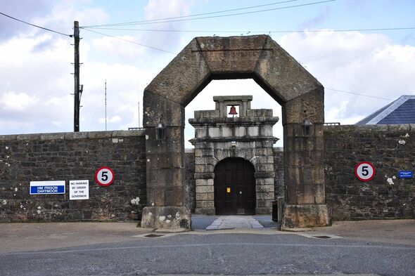 An image depicting an ancient stone archway, constructed from gray stone, situated in the middle of a paved street. The archway 