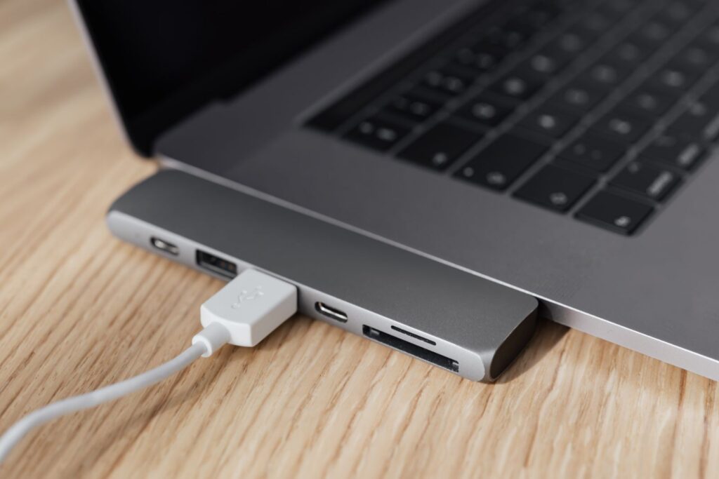 Angle élevé d'un ordinateur portable argenté moderne avec hub multiport USB de type C et câble blanc branché placé sur une table en bois