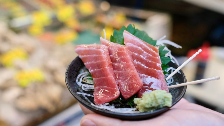 Una mano sujetando el tartar de pescado en el mercado exterior de Tsukiji, Japón