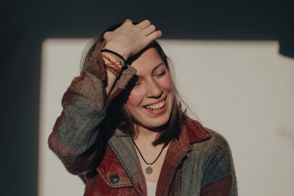 A happy woman is laughing holding her head in the natural sunlight indoors.