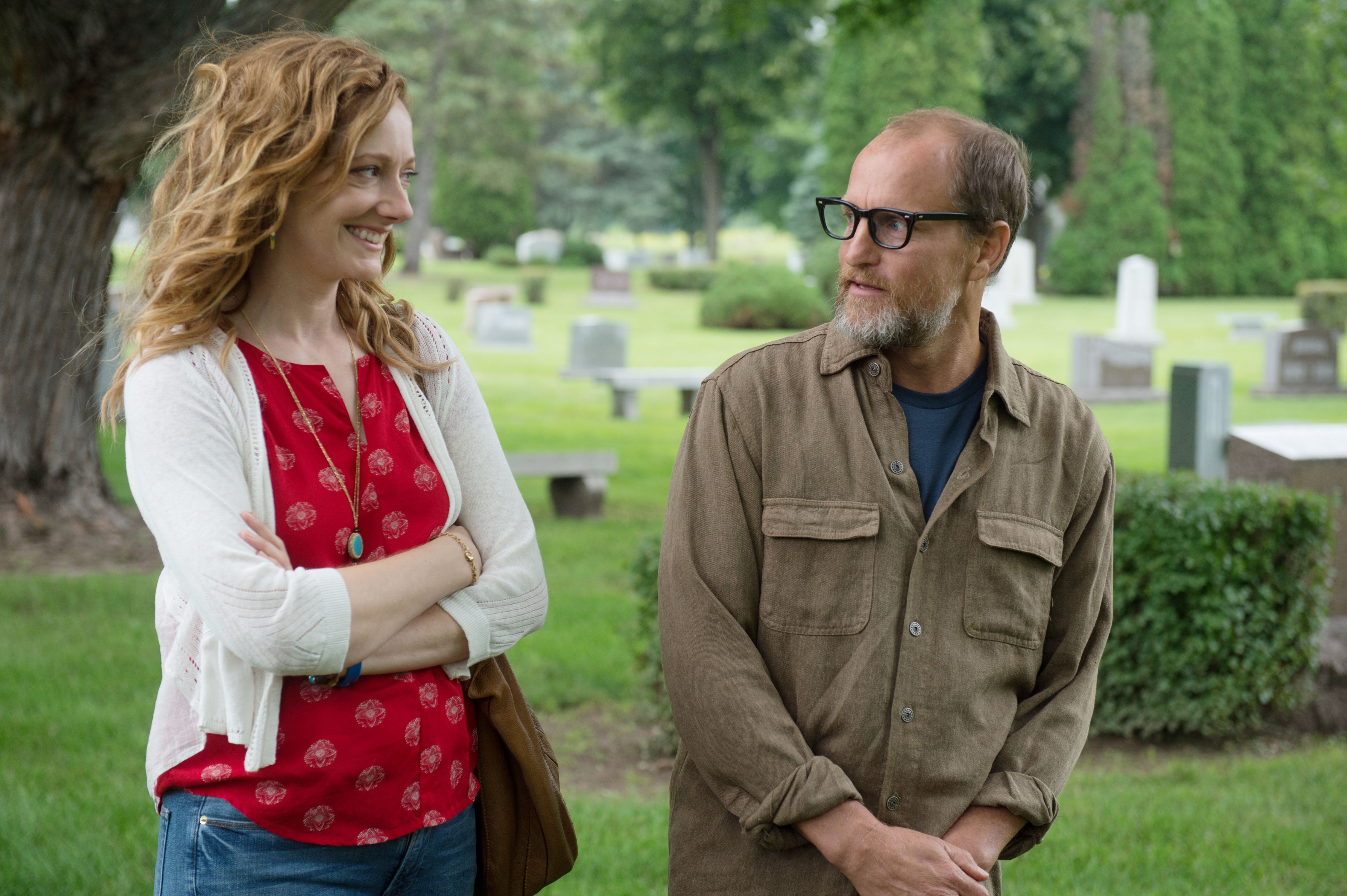 Judy Greer and Woody Harrelson walk and converse in a cemetery