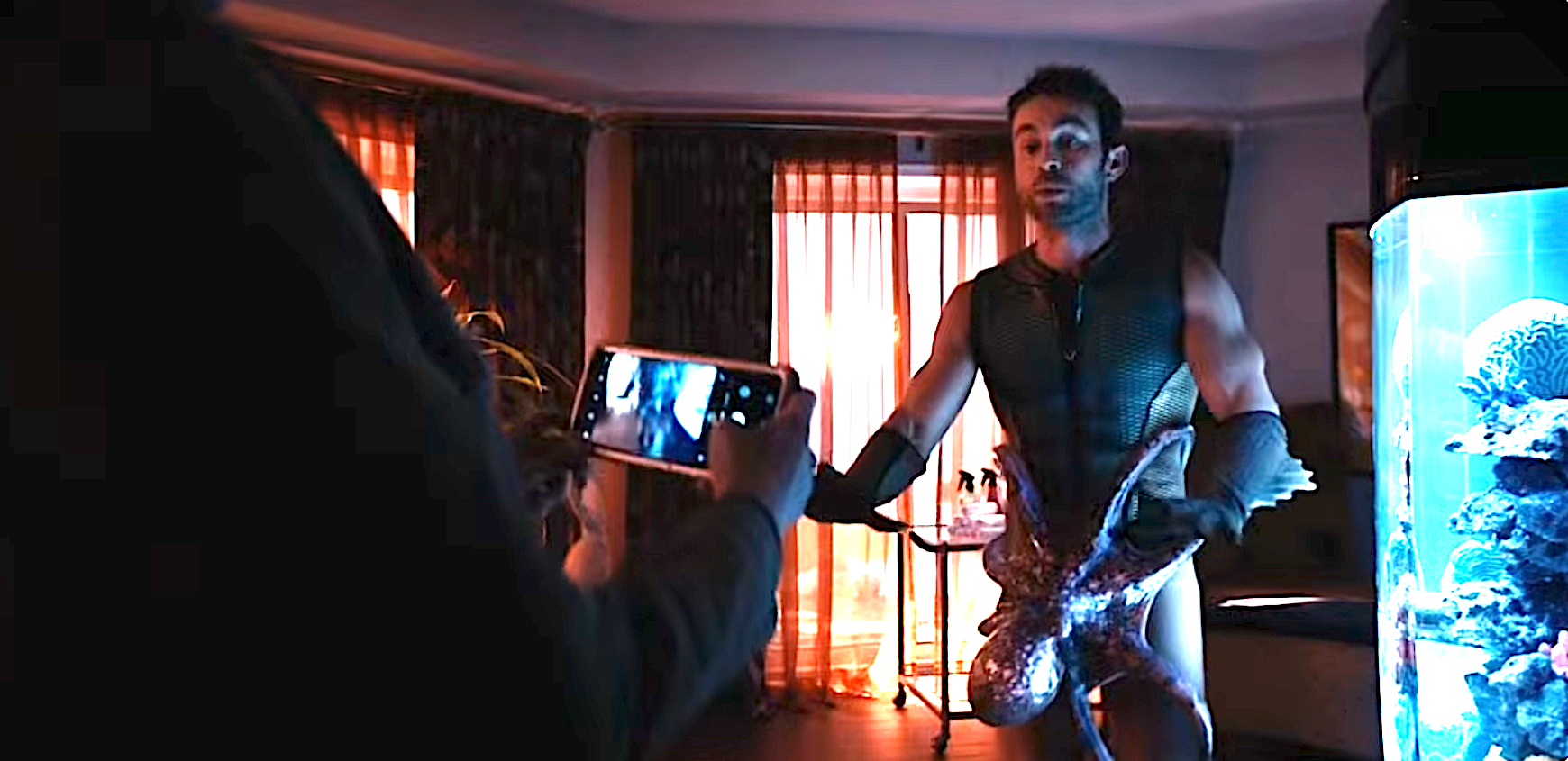 Chace Crawford, in a superhero costume, is recorded having sex with an octopus by someone with a smartphone inside a room with large windows and an aquarium