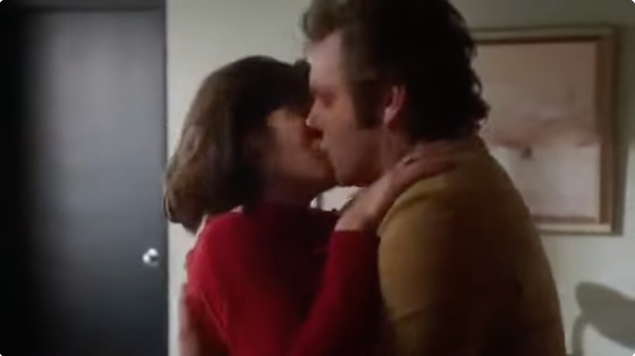 Lizzy Caplan and Michael Sheen are sharing a kiss in a close embrace indoors