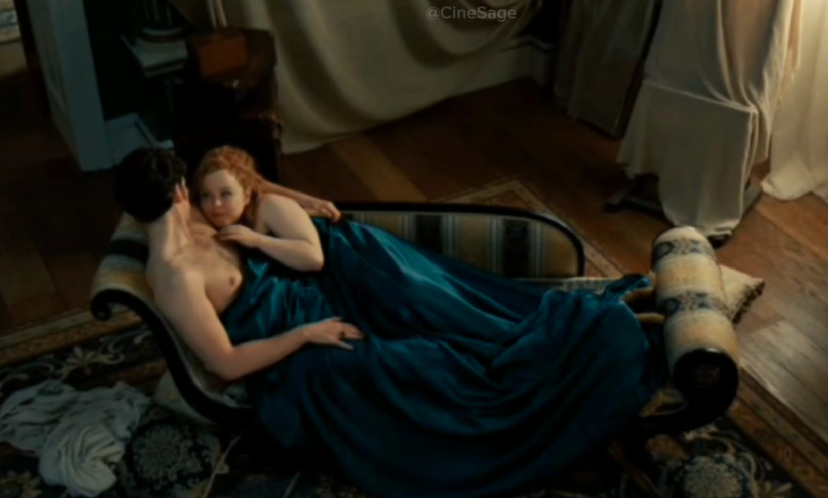 Nicola Coughlan and Luke Newton are lying together on a chaise lounge covered by a blanket