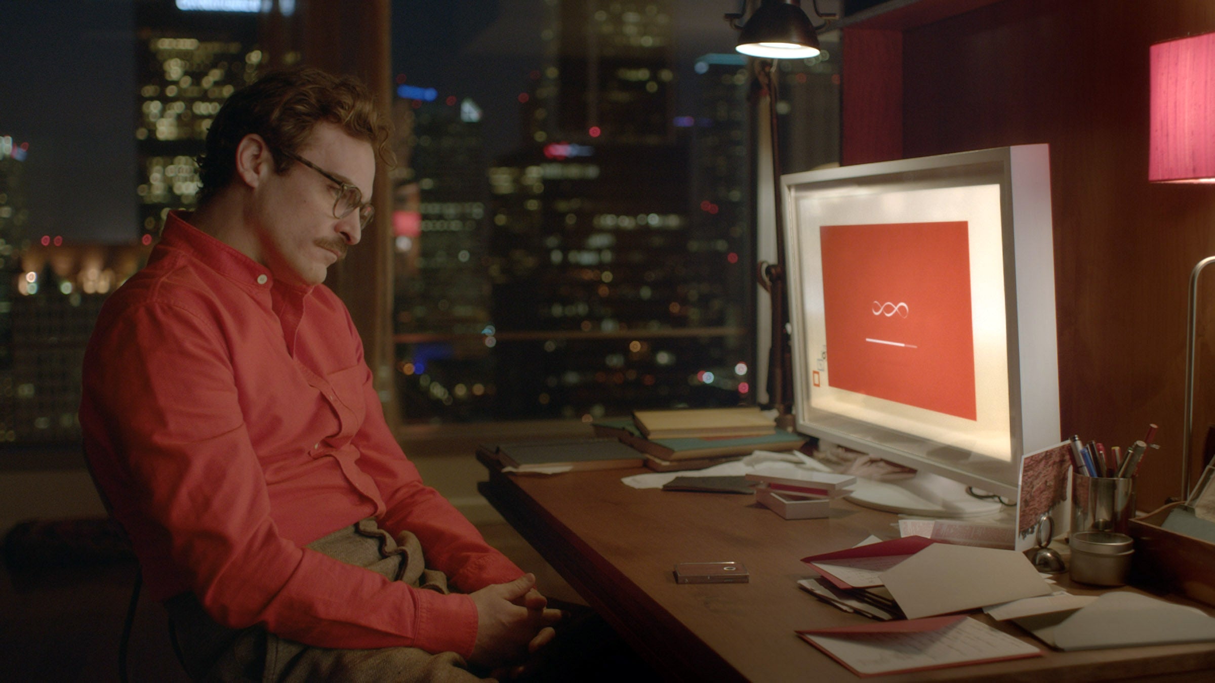 Joaquin Phoenix sits at a desk in a city apartment, gazing at a computer screen