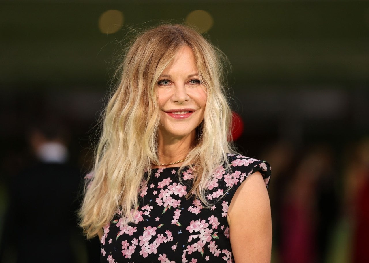 Meg Ryan smiling in a black and pink floral cap sleeved dress. - 