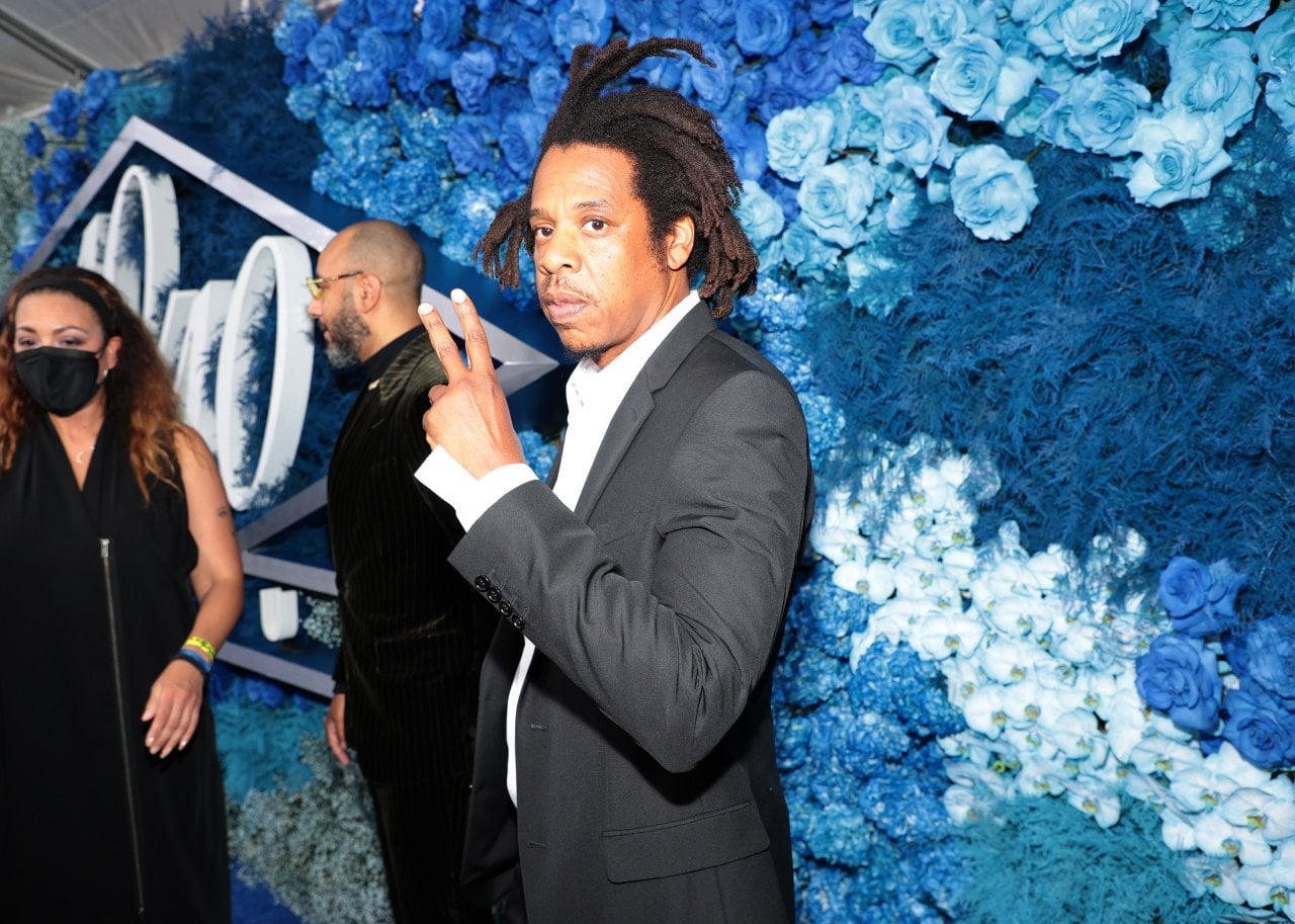 Jay-Z gives the peace sign in front of a wall of blue flowers. - 