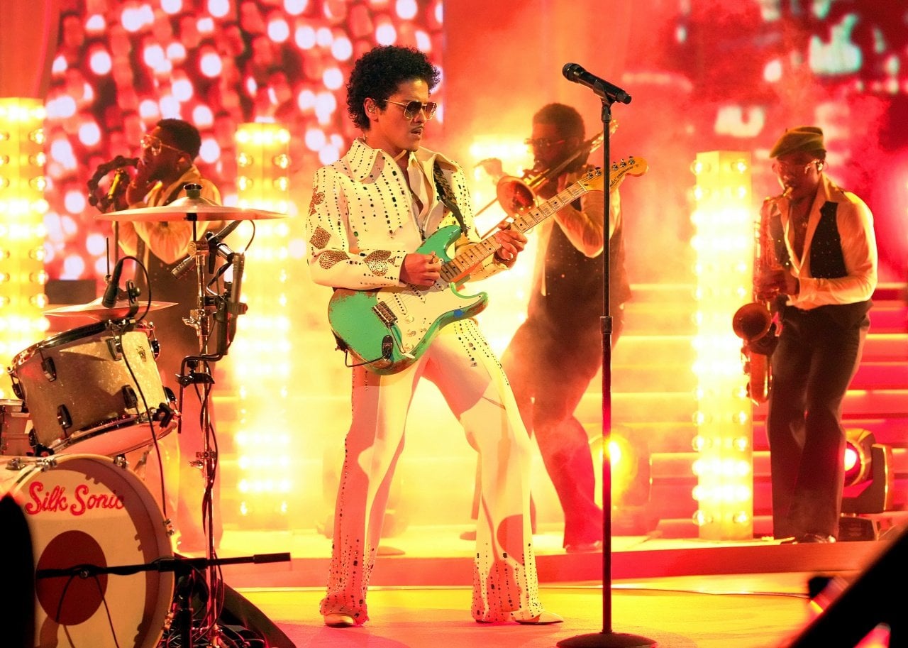 Bruo Mars and his band perform onstage engulfed in golden light. - 