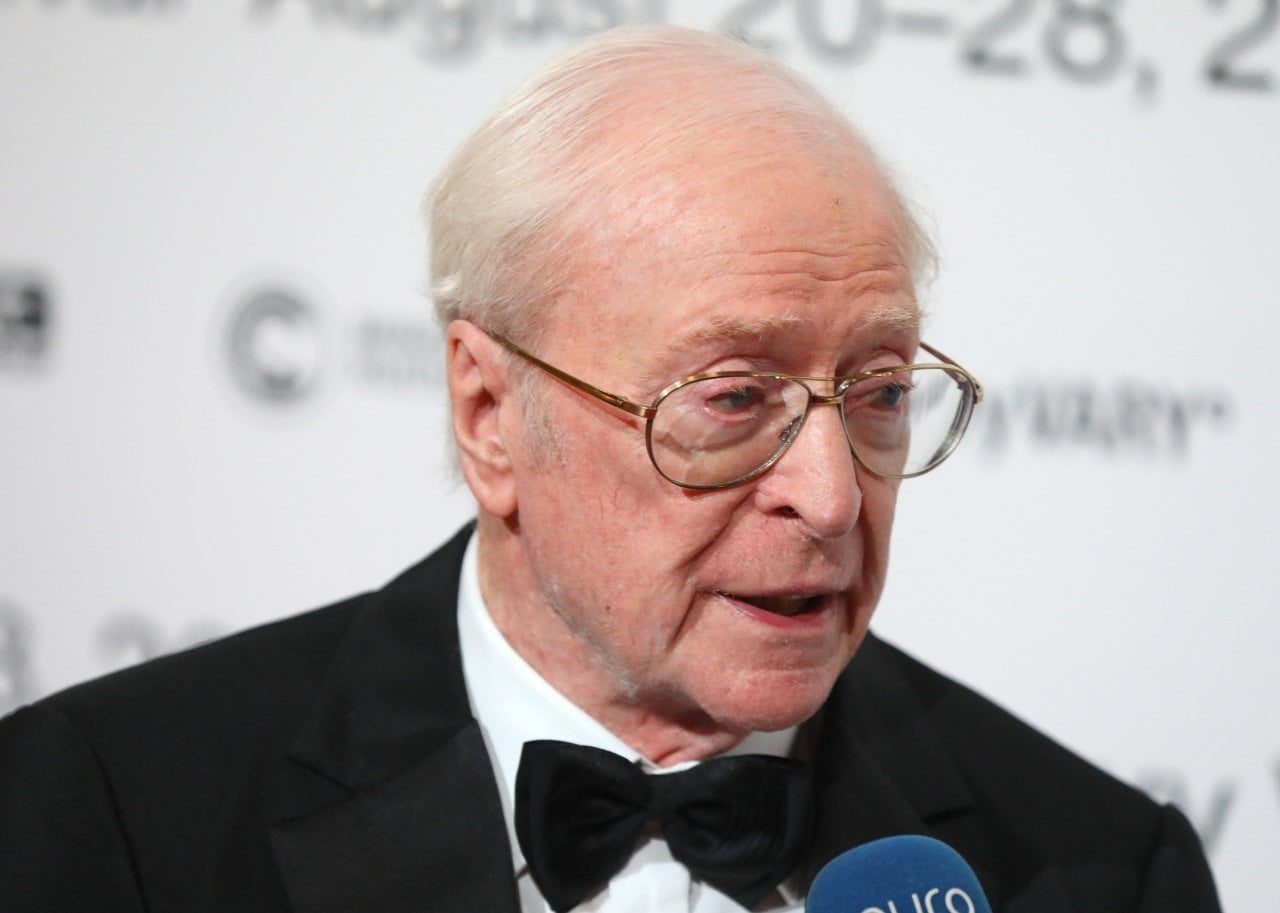 Michael Caine is interviewed at an event wearing a black suit. - 