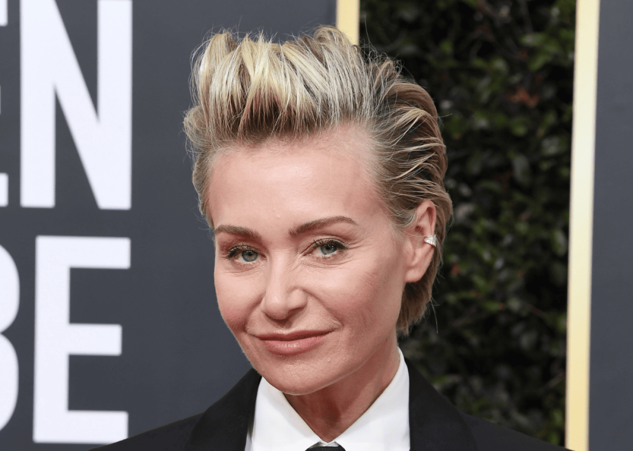Portia de Rossi smiles wearing a black suit and tie. - 