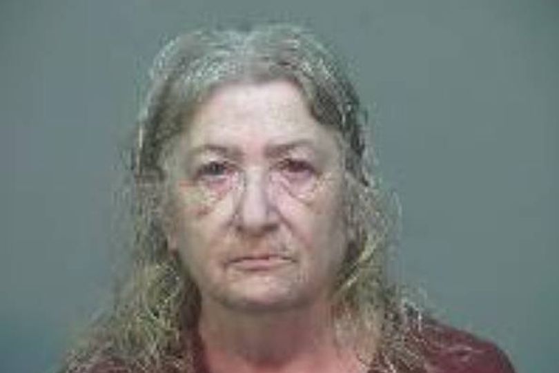 An individual with long, unkempt hair and a solemn expression stands against a plain, gray background, likely in a law enforcement setting.