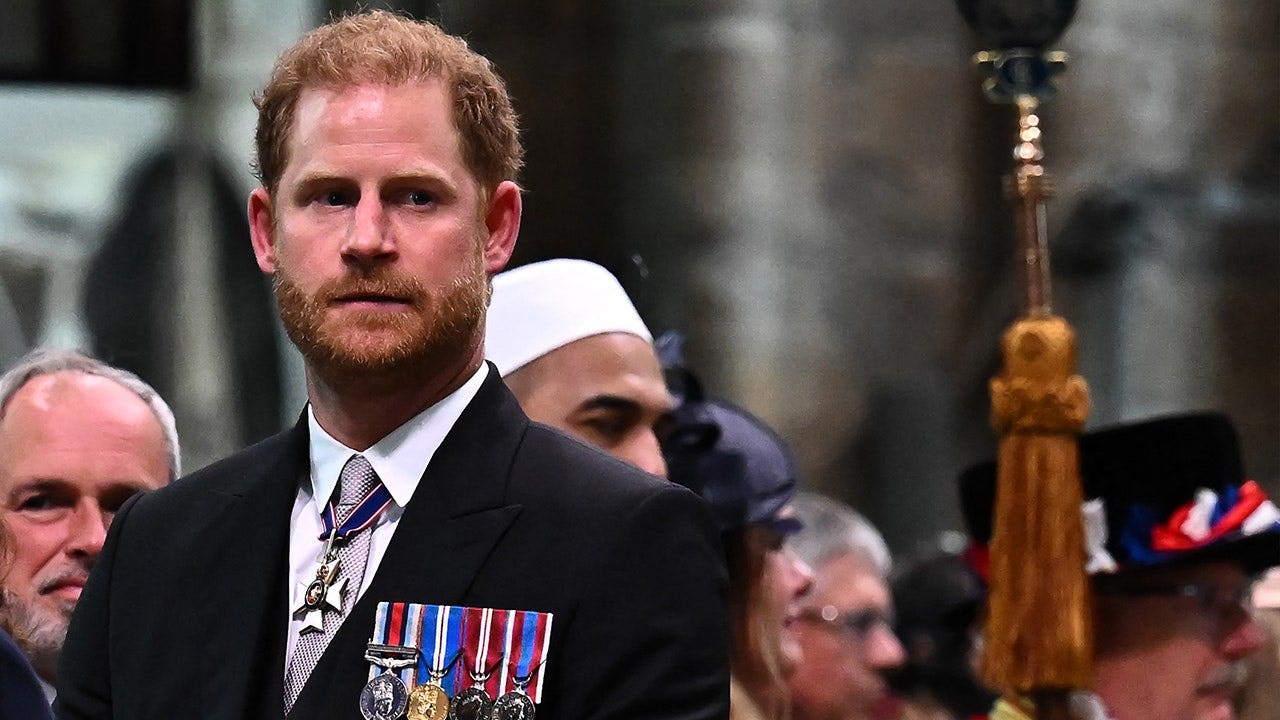 El Príncipe Harry con traje oscuro y medallas mirando hacia arriba durante la ceremonia de coronación de su padre.