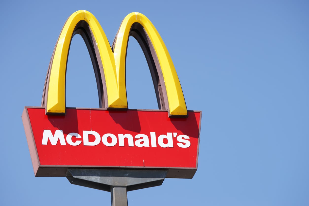 McDonald’s outdoor sign with the iconic yellow “M” arches on top of a red background with white text spelling “McDonald’s,” set against a clear blue sky.
