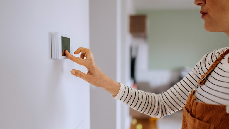 A person operating the smart thermostat placed on the wall of her house