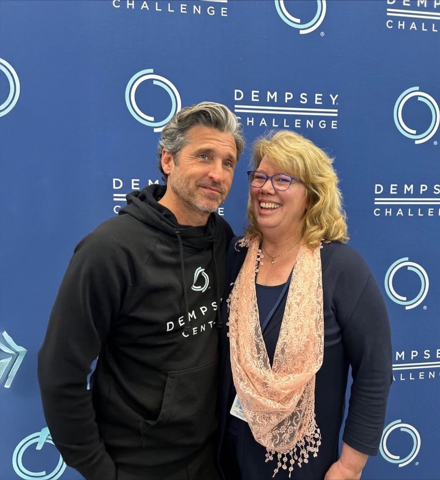 Um homem de preto "Centro Dempsey" moletom com capuz fica ao lado de uma mulher sorridente de óculos e lenço rosa, na frente de um "Desafio Dempsey" pano de fundo.