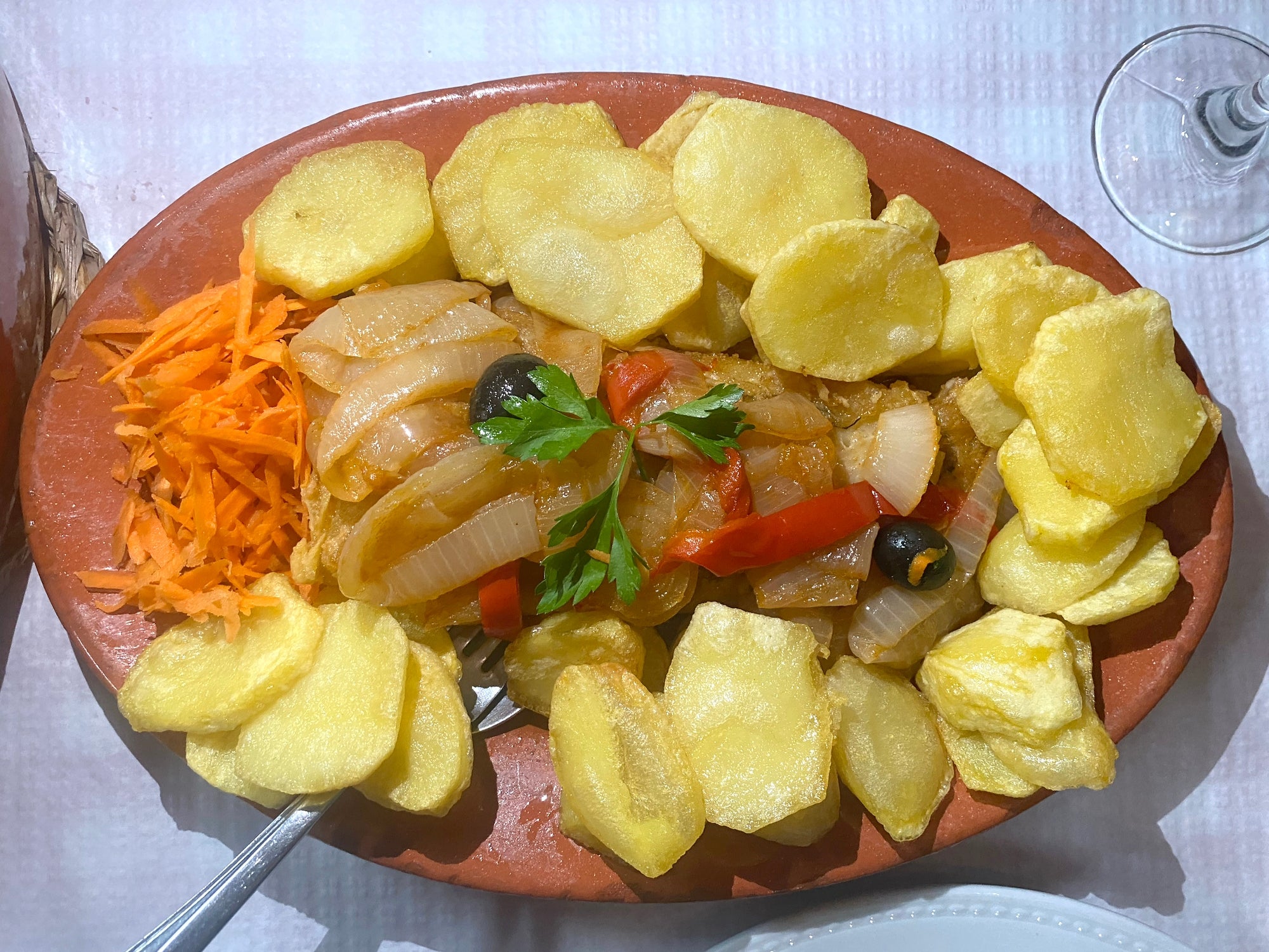 Prato com peixe coberto com legumes, guarnecido com salsa, rodeado de batatas fatiadas e cenouras raladas em um prato oval
