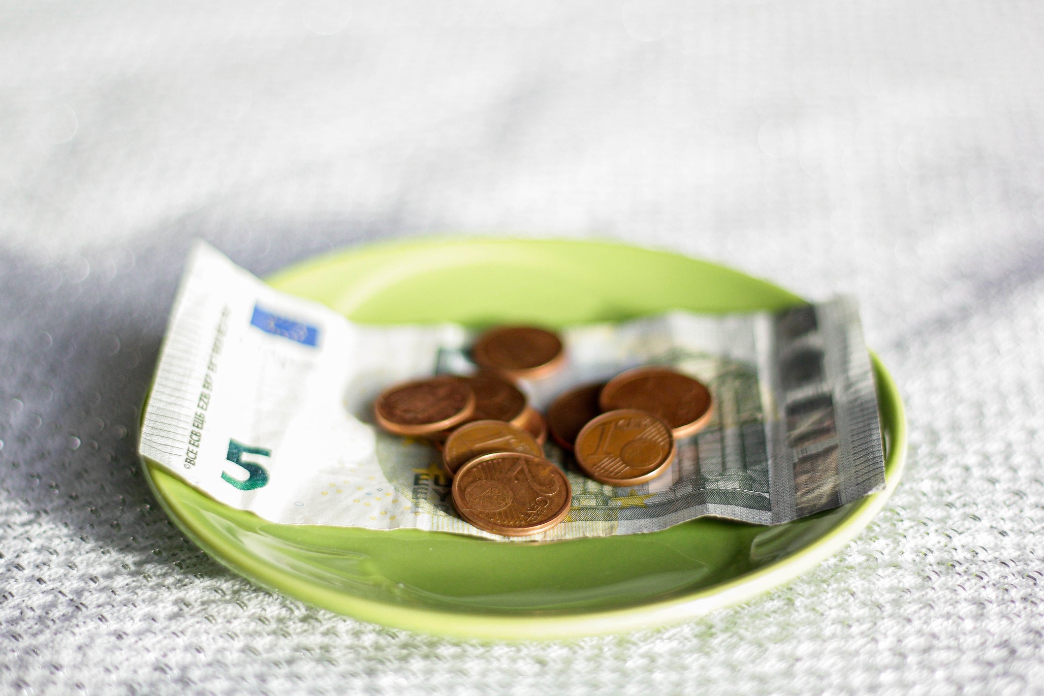 Moedas de euro e uma nota de cinco euros numa placa verde, sugerindo despesas de viagem ou poupanças