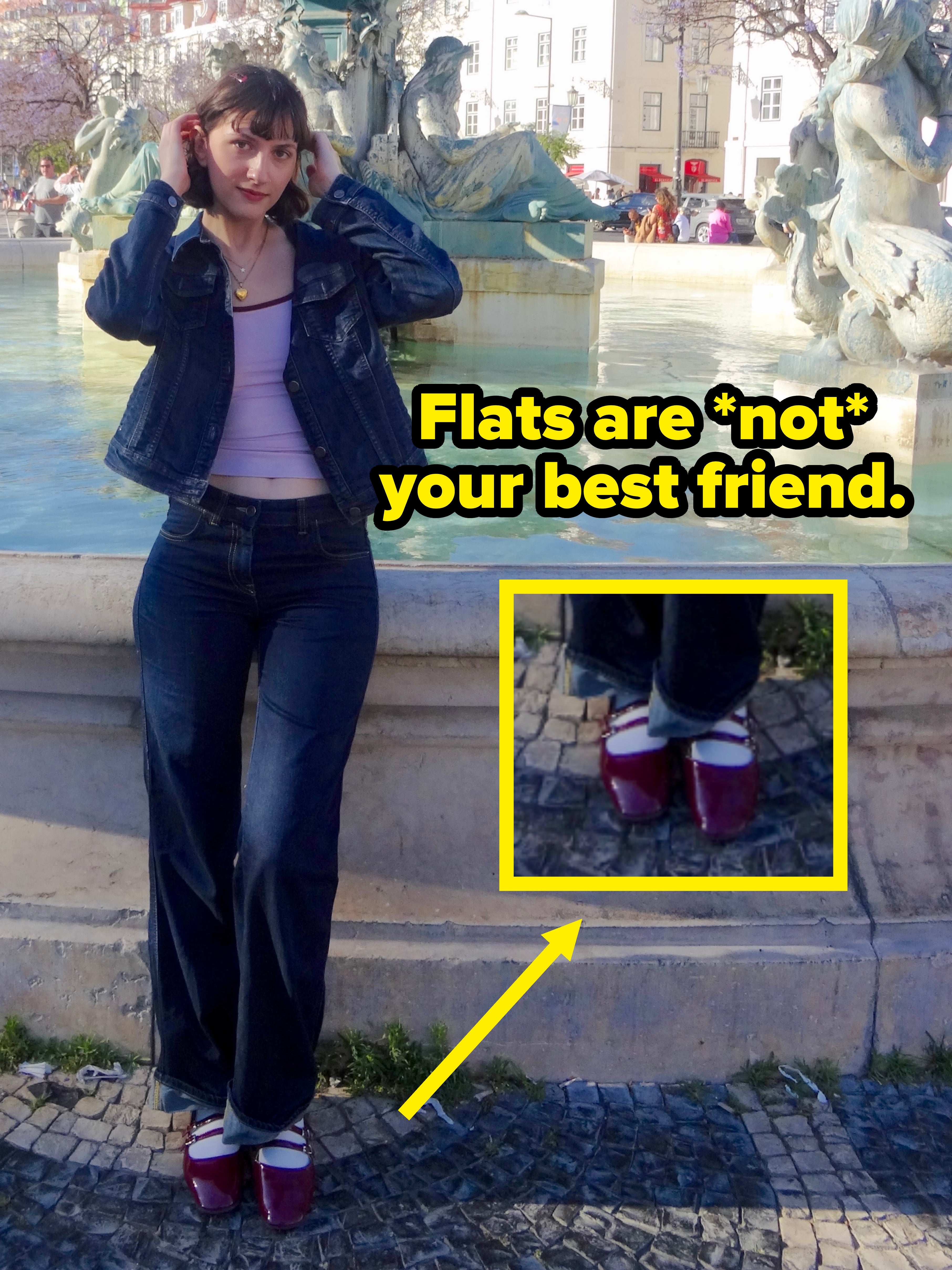Mulher posa em frente a uma fonte histórica em uma praça da cidade, vestindo uma jaqueta jeans e jeans. Prédios e um céu claro estão ao fundo