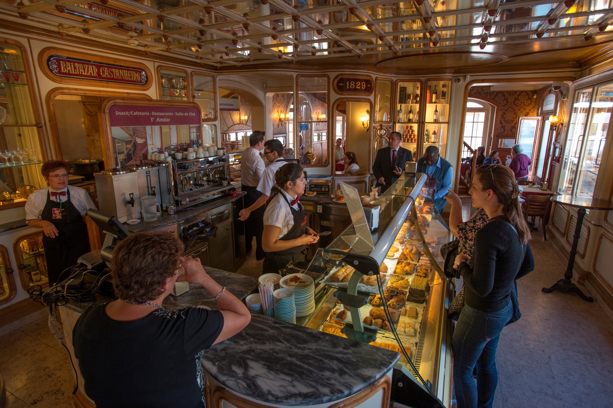 Pessoas fazendo pedidos em um movimentado café italiano com interior vintage e exposição de doces, capturando uma experiência clássica de café europeu