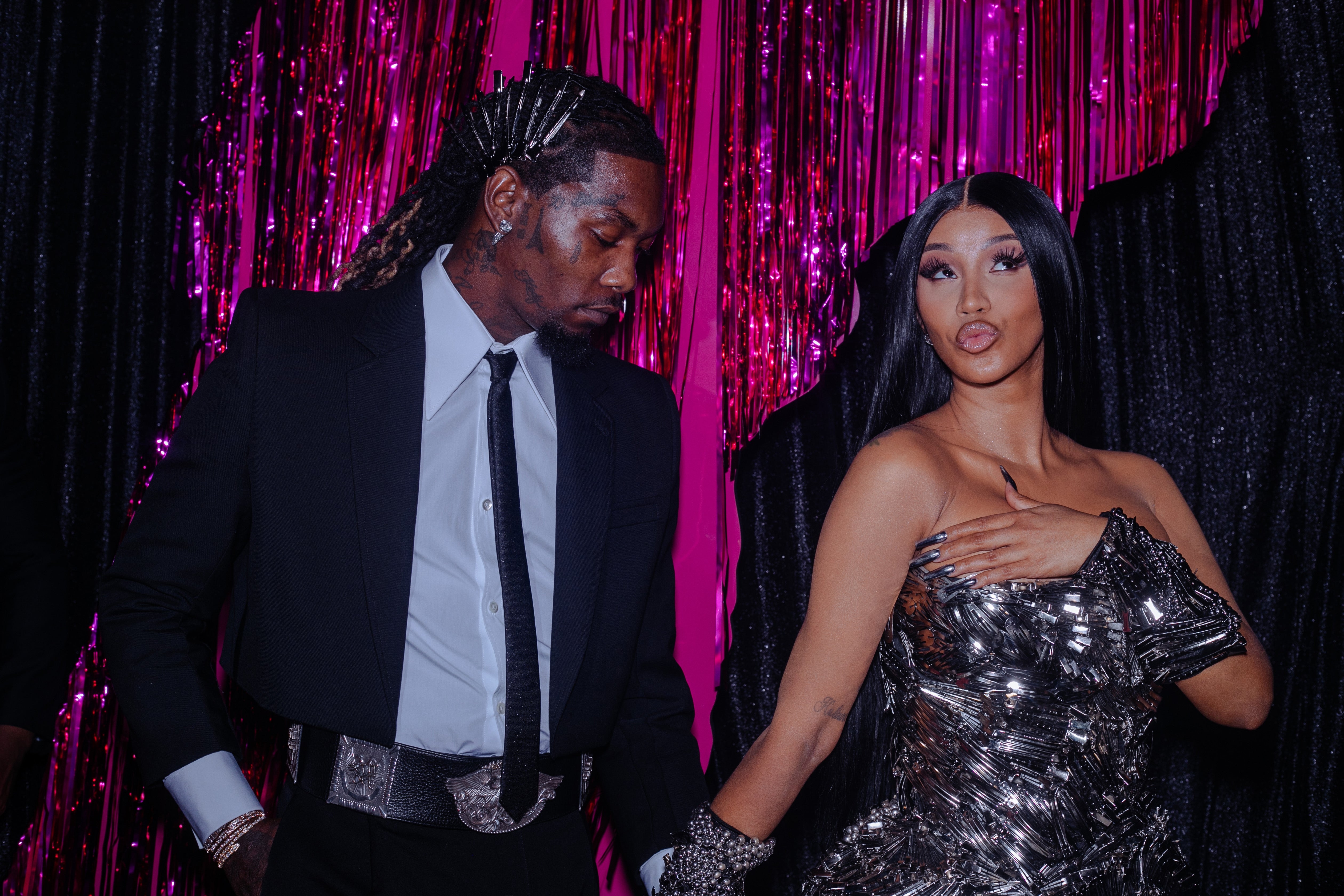 Offset wears a suit and holds Cardi B's hand. Cardi B wears a silver, sparkling gown and strikes a playful pose