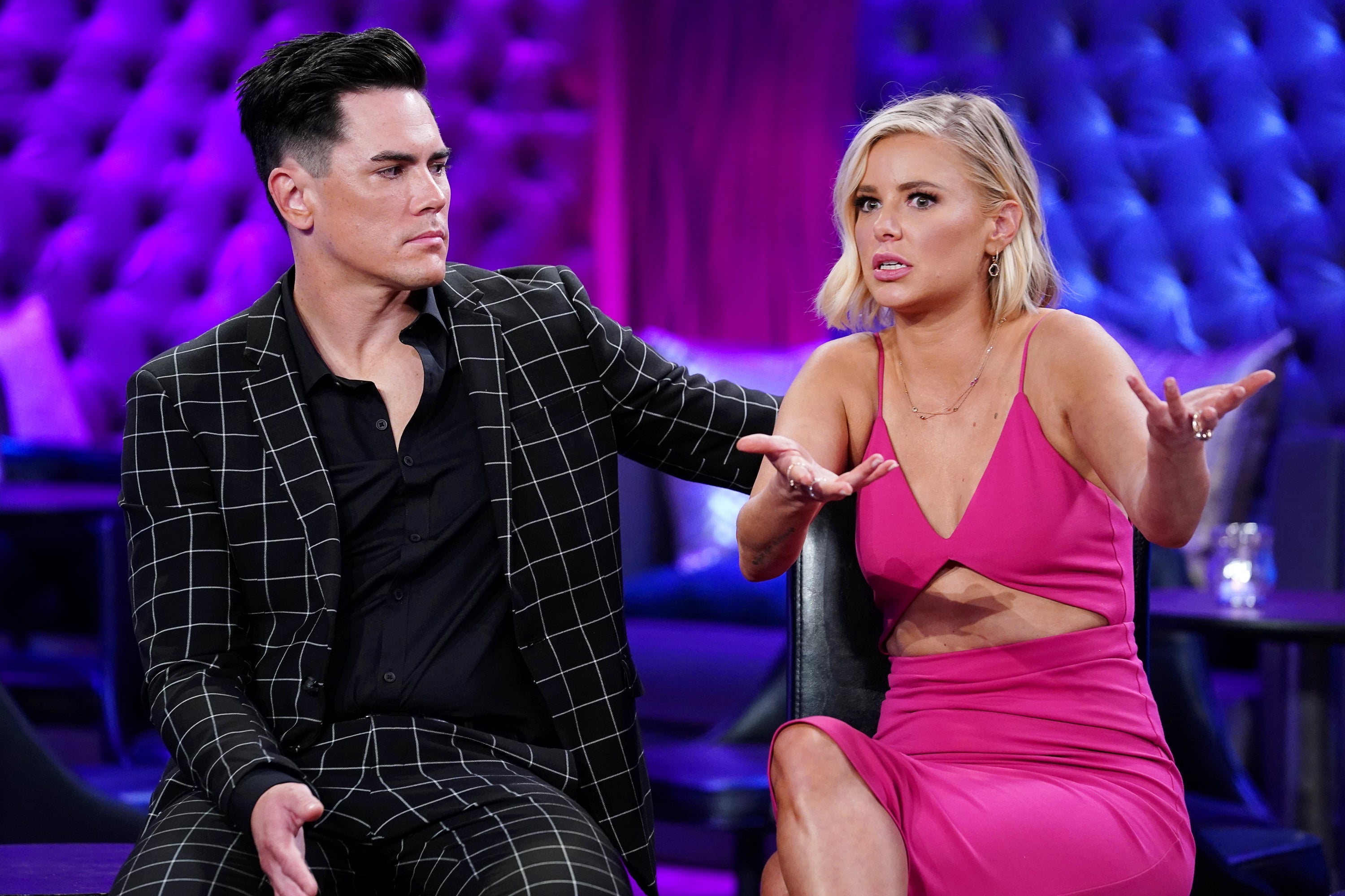 Tom Sandoval wears a black patterned suit and sits beside Ariana Madix, who wears a hot pink dress. Ariana Madix holds her hands up and looks confused