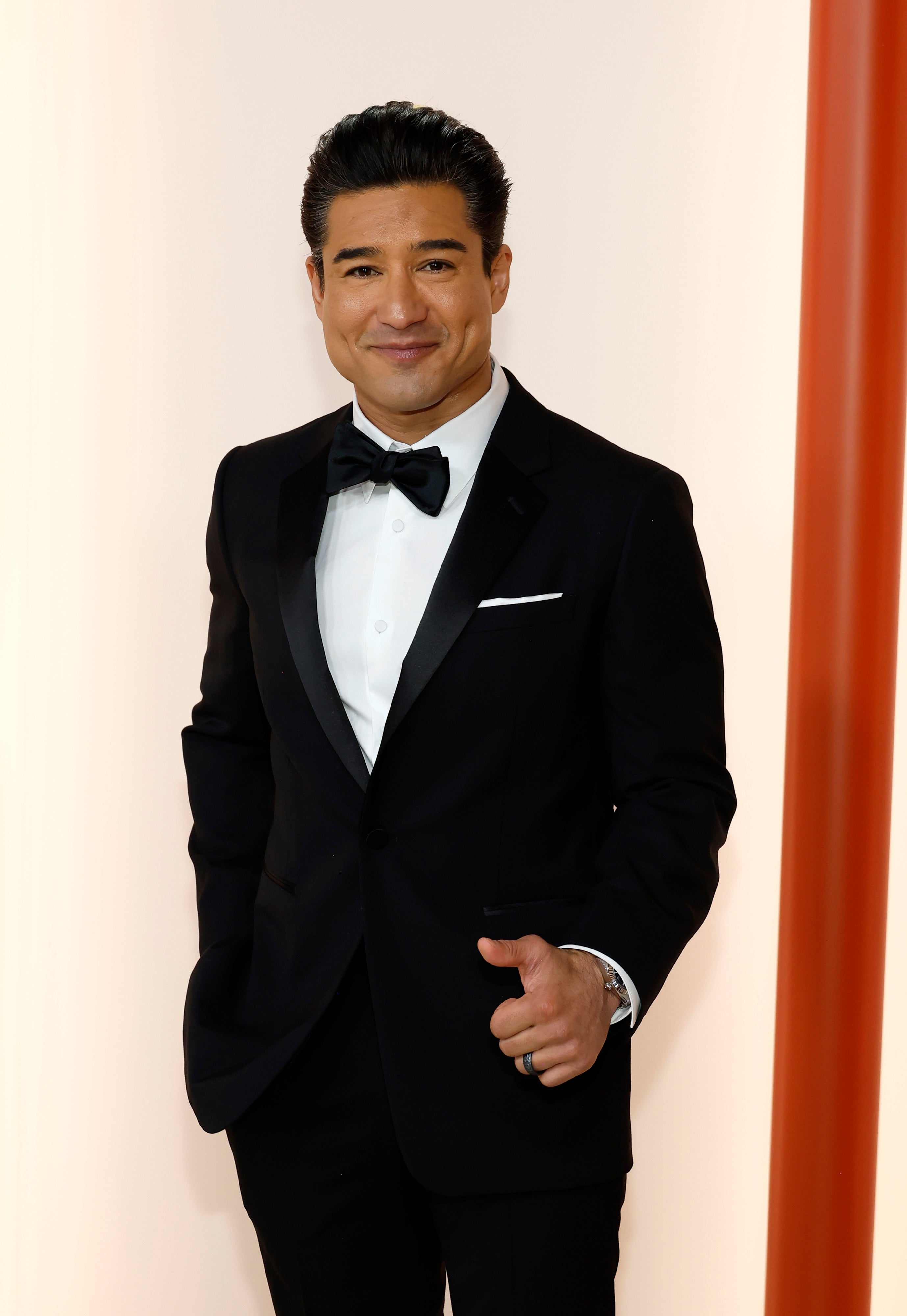 Mario Lopez wears a tuxedo and puts his thumb up while slightly smiling