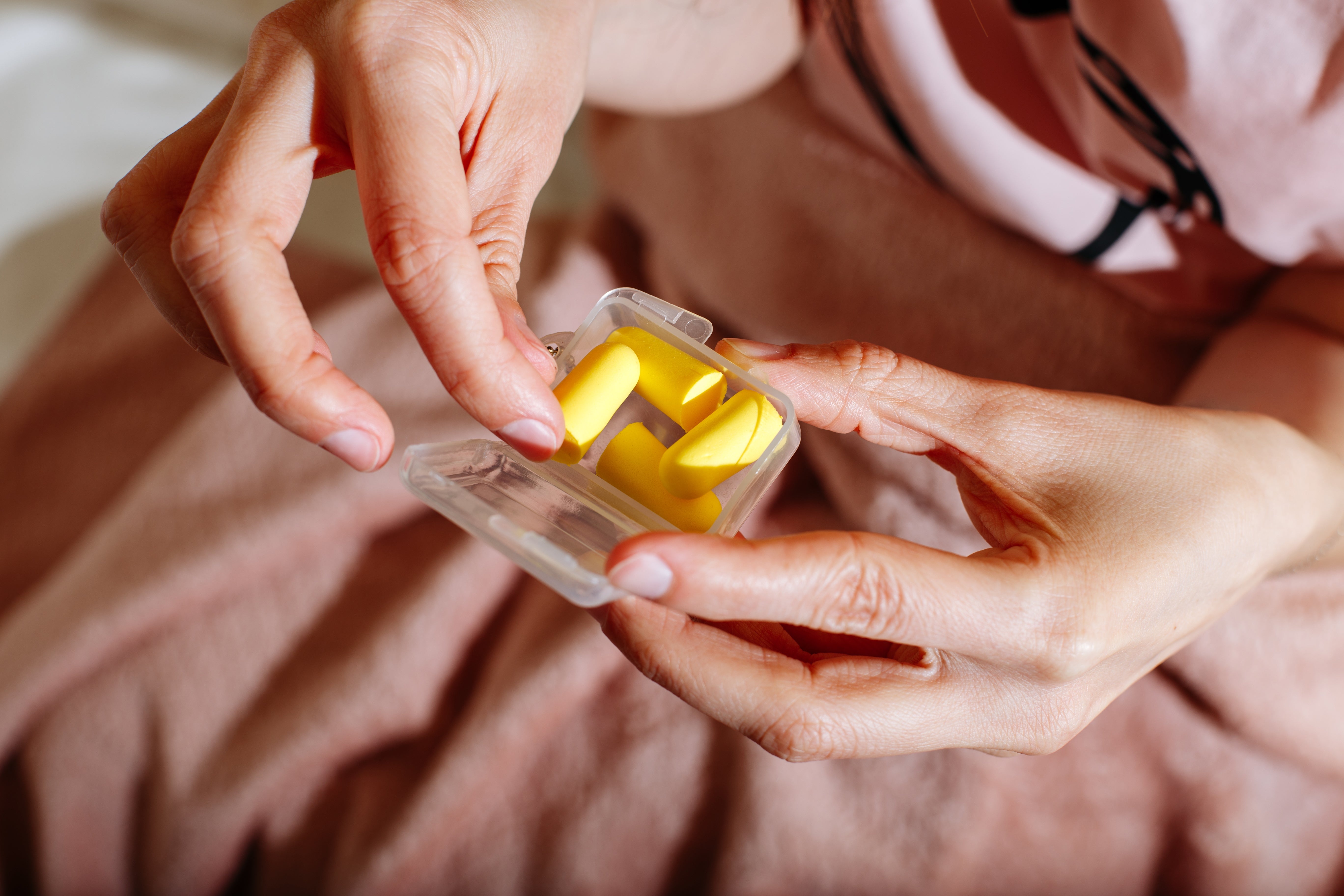 A person holding a clear case with yellow earplugs