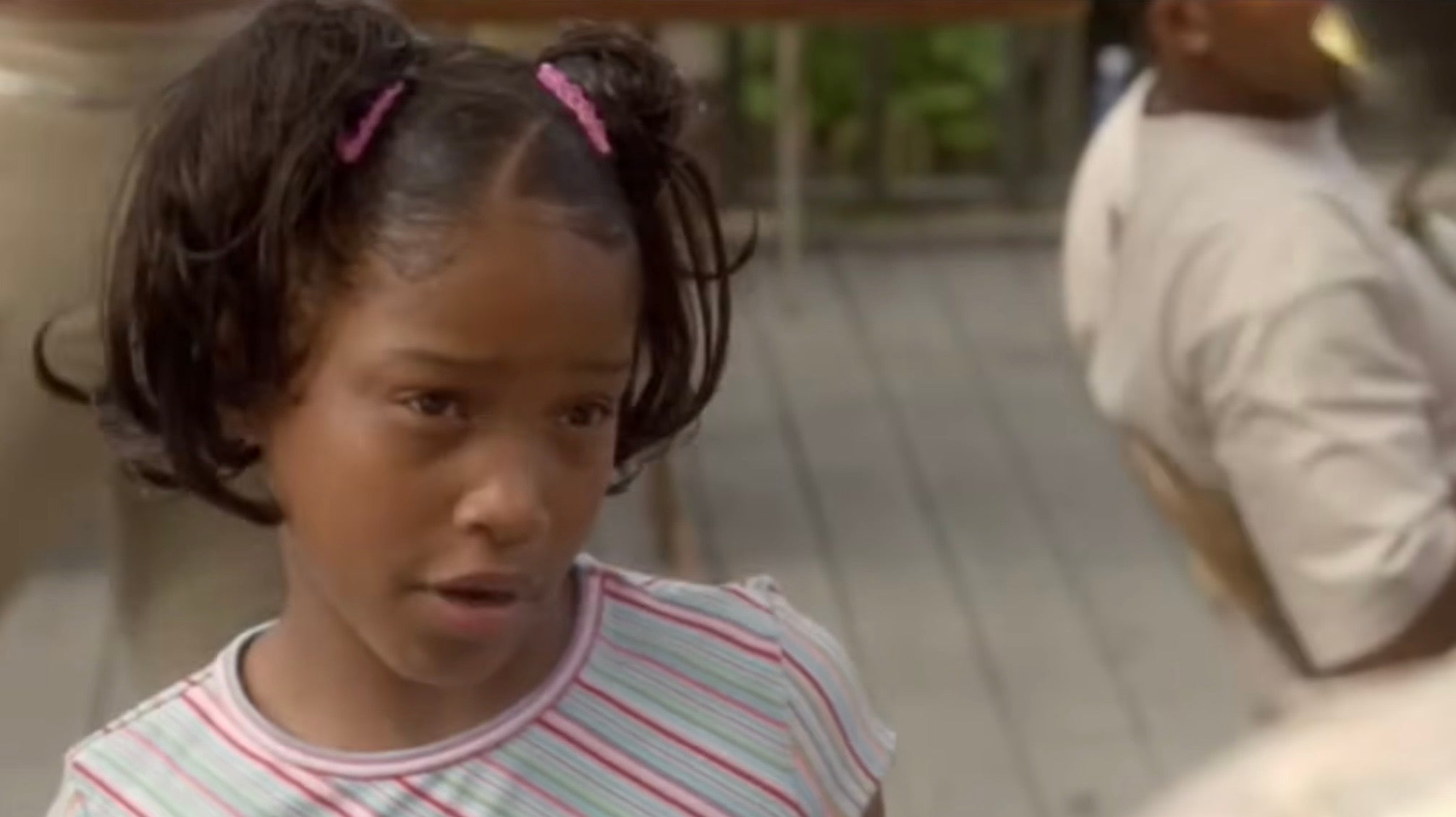 Young Keke Palmer with pigtails, wearing a striped shirt, looking serious while outdoors