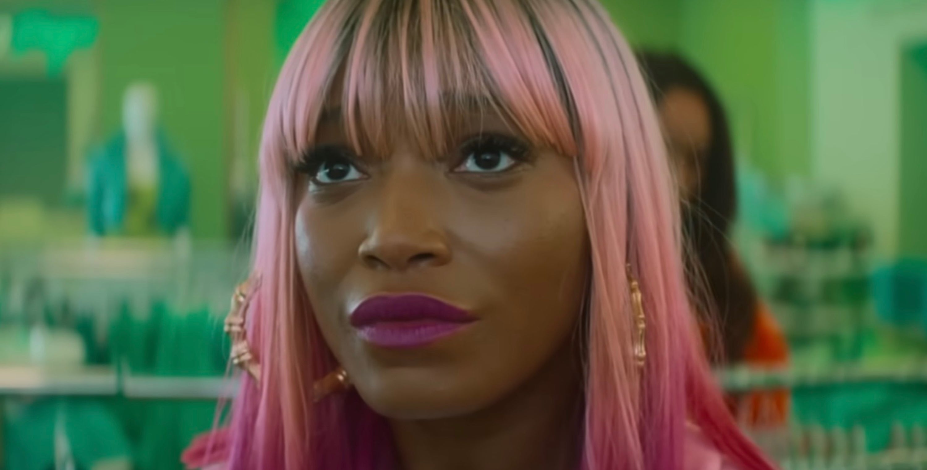 Keke Palmer with pink hair and hoop earrings looking upwards inside a store