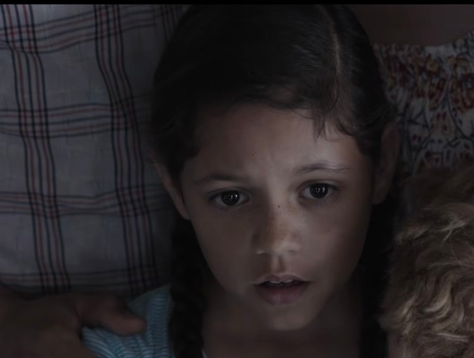 A young Jenna Ortega with braided hair looks ahead, appearing focused and thoughtful, surrounded by adults
