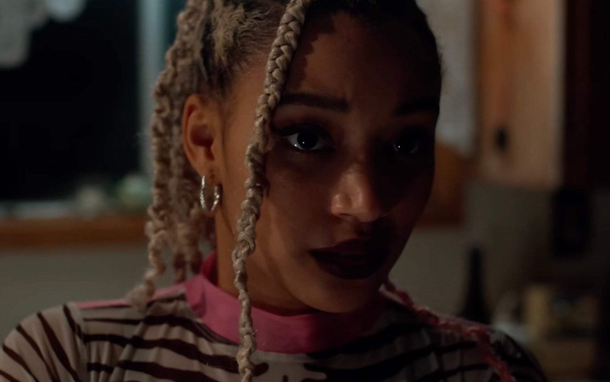Amandla with braided hairstyle in a patterned top, looking thoughtfully in a dimly lit setting
