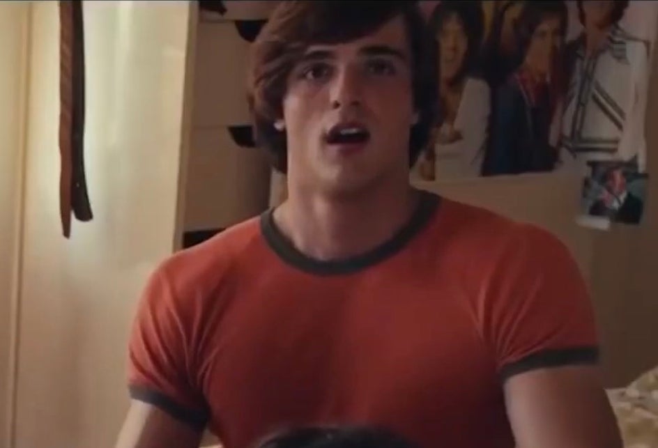 Jacob Elordi in a fitted t-shirt with a surprised expression in a room with posters on the wall