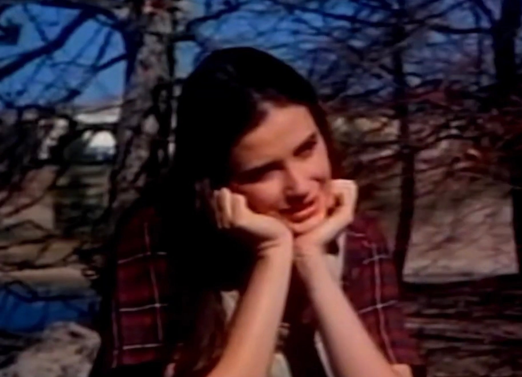 Demi Moore outdoors rests their chin on their hands, appearing thoughtful, with trees and a blurred background behind them