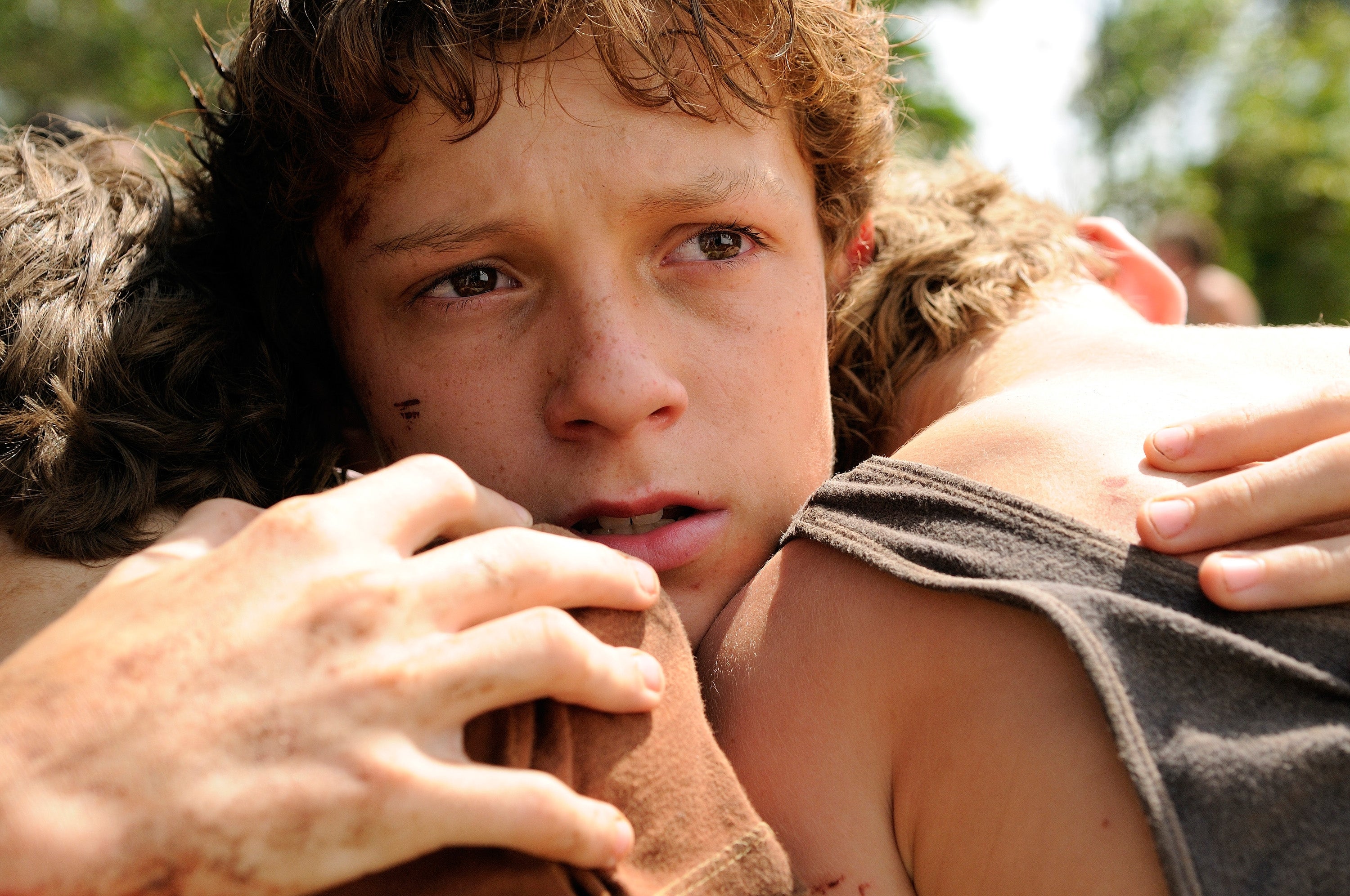 Young Tom Holland with a worried expression hugs two others tightly, showing an intense emotional moment