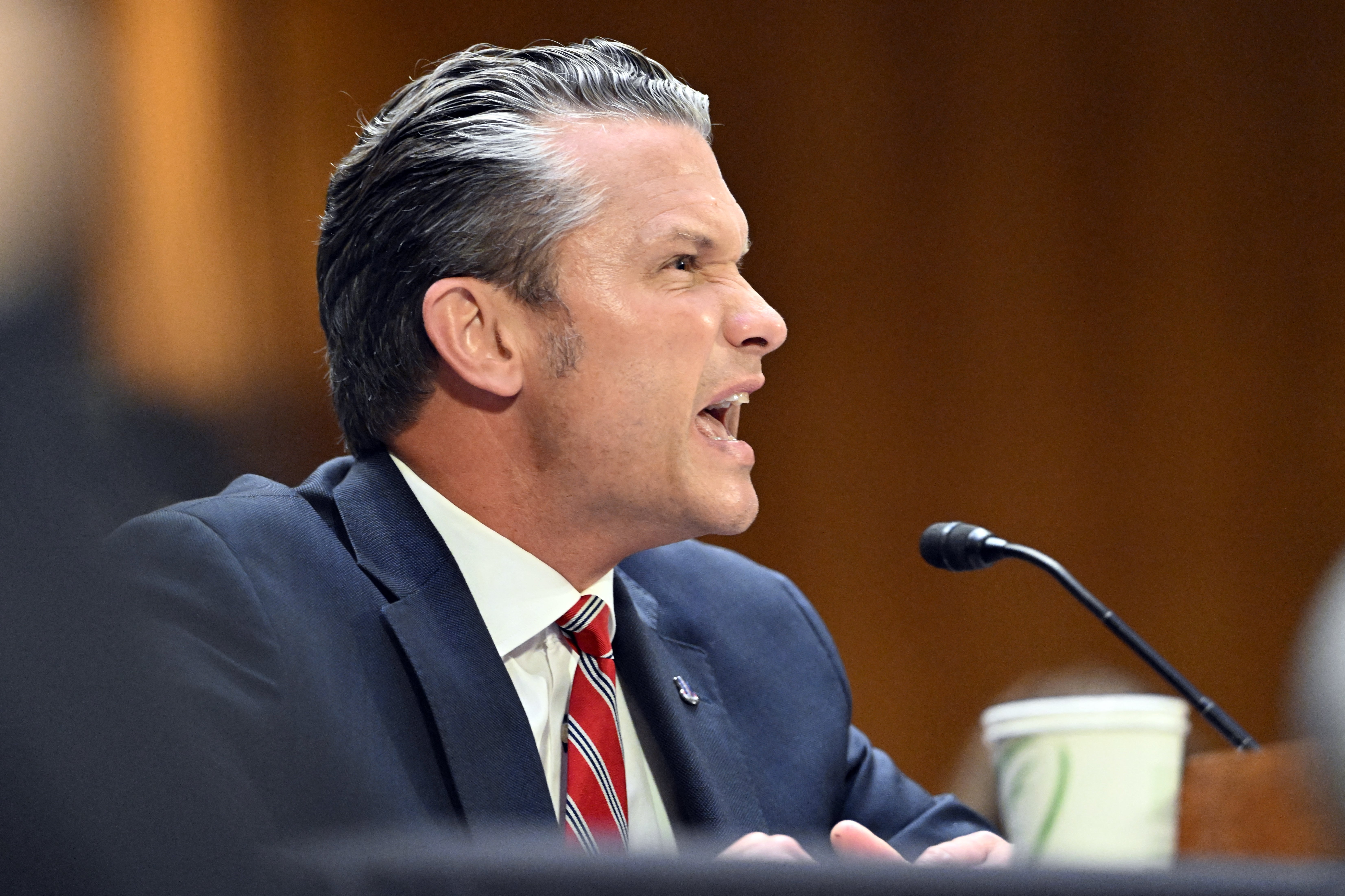 A man in a suit speaks passionately into a microphone at a formal event or hearing
