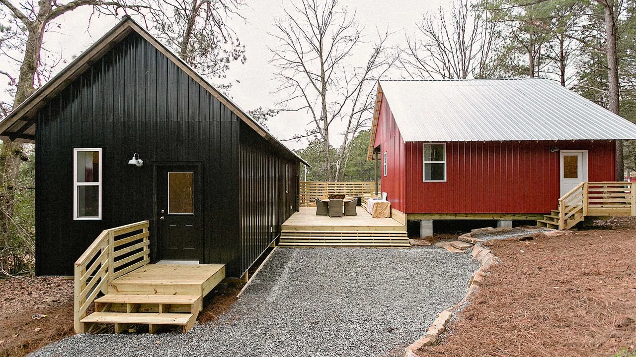 Deux petites maisons, une noire et une rouge, avec des porches et des marches en bois, se dressent au milieu des arbres. Un chemin de gravier mène aux maisons et des sièges extérieurs sont disposés sur le pont reliant.