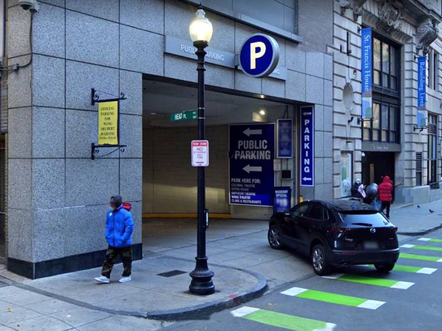 Une entrée de parking public avec un bleu "P." panneau, une voiture noire garée sur le trottoir, des piétons à proximité et des pistes cyclables à rayures vertes peintes dans la rue.