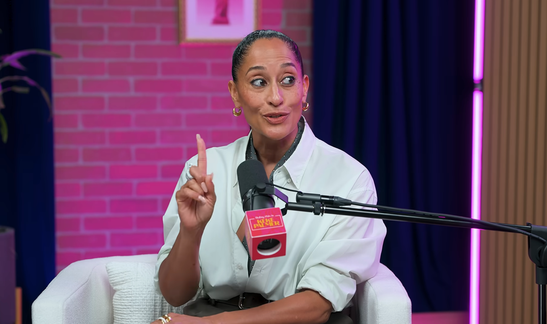 Persona sentada en un estudio de podcast, hablando por un micrófono, vestida con una camisa informal con botones