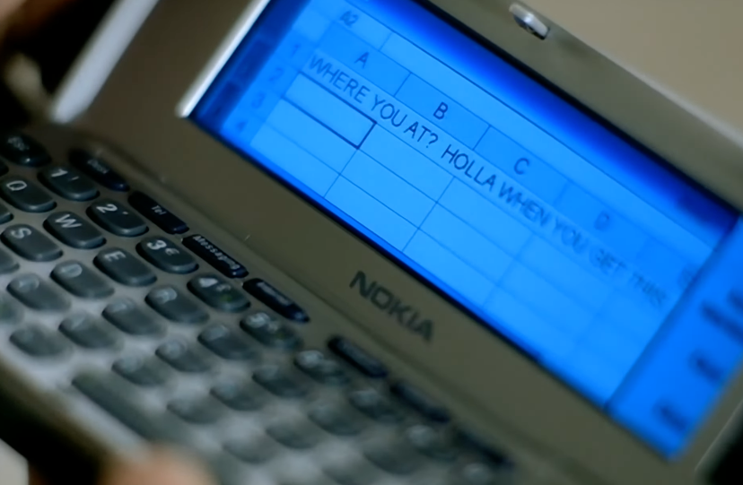 Close-up of a Nokia phone screen displaying a text in a spreadsheet: "WHERE YOU AT? HOLLA WHEN YOU GET THIS."