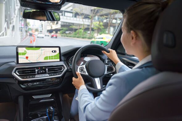 Back view of young female driver sitting at steering wheel and looking GPS navigation screen during road trip.