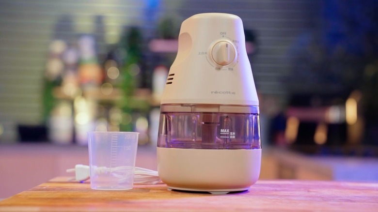 A beige-colored rice polisher with an empty measuring cup beside it