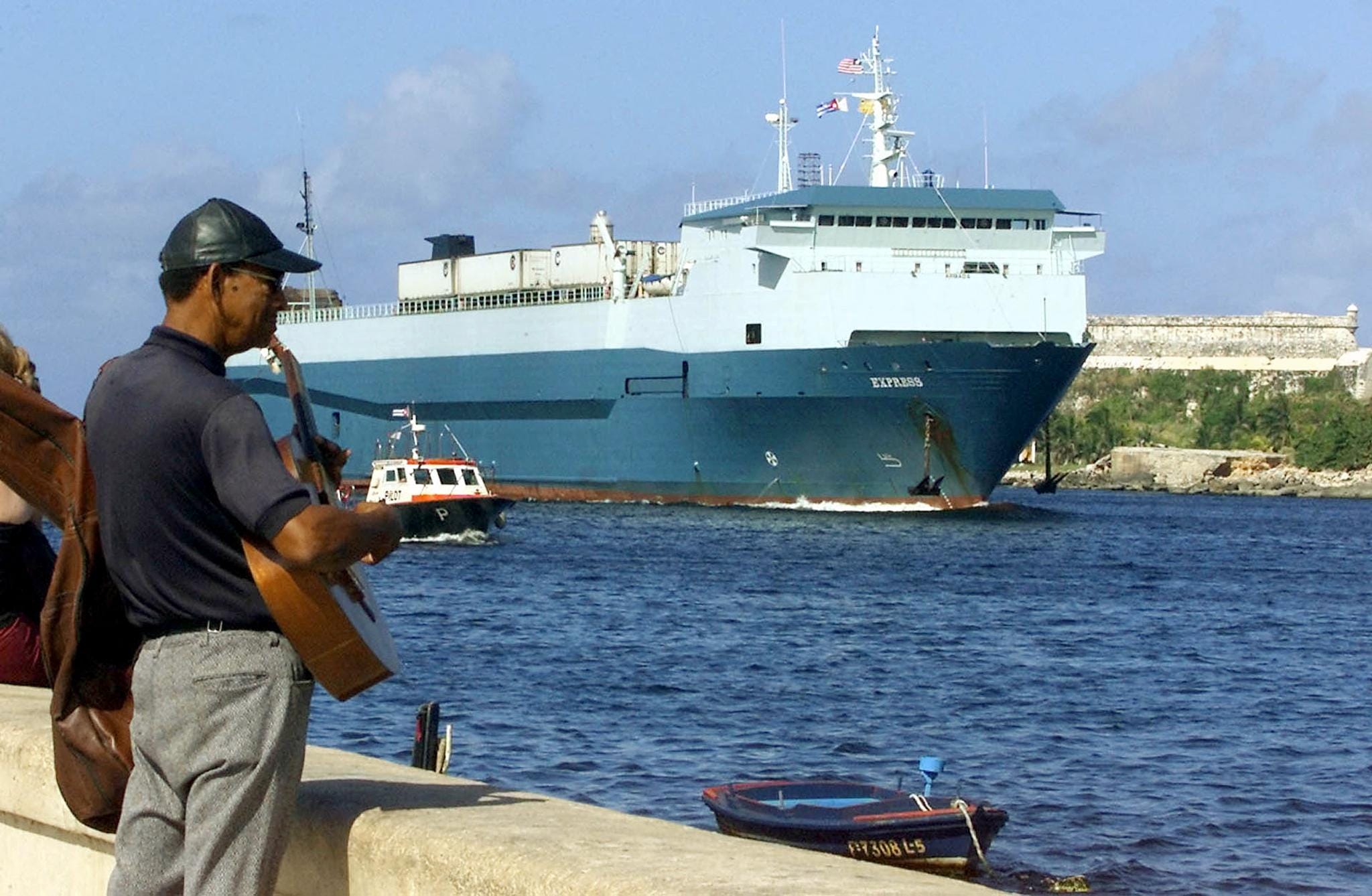 A street musician plays in Havana, Cuba, as a container vessel arrives in 2001 with supplies shipped from Gulfport, Mississippi.