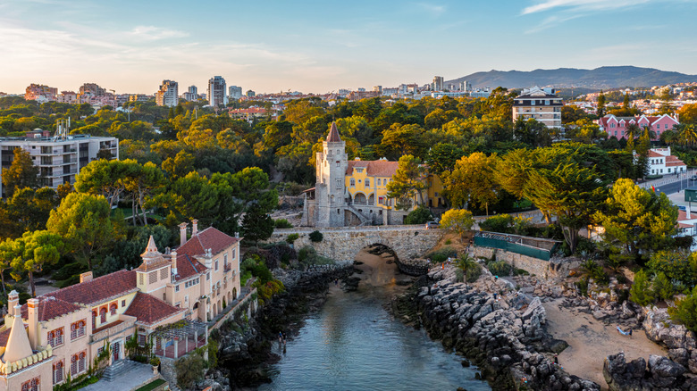 Wide shot of ancient buildings, lush greenery, tidal pool in the center at sunset