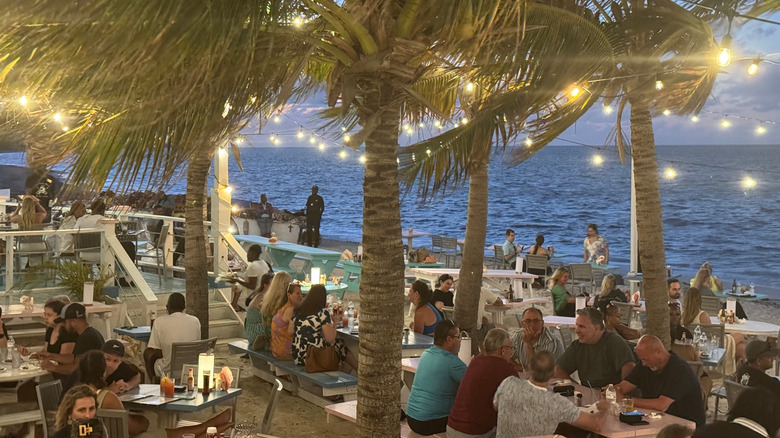 Restauracja i bar rumowy Da Conch Shack ze stolikami z widokiem na ocean na piasku i palmami ozdobionymi lampkami