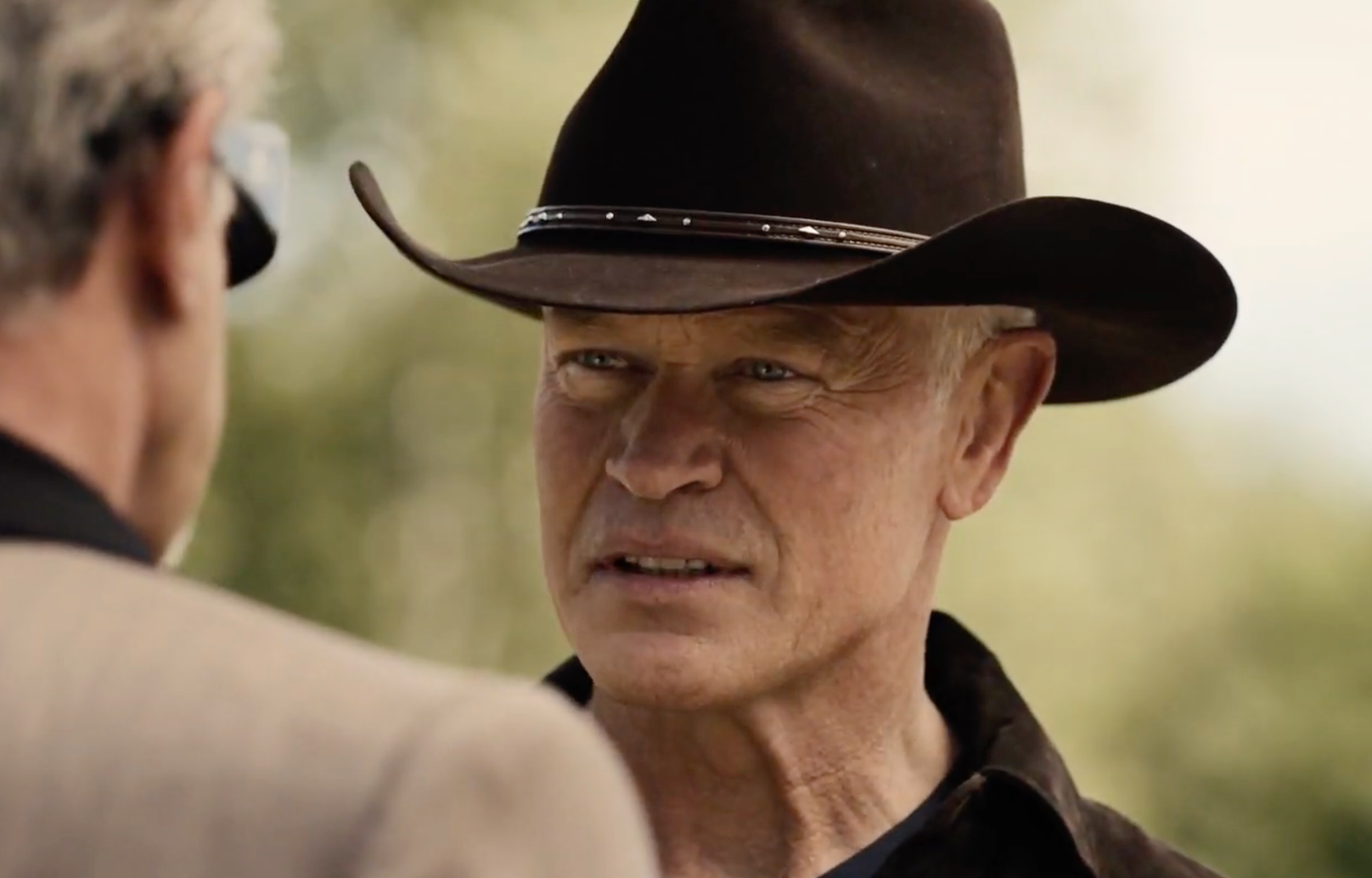 Man with a cowboy hat engaged in a serious conversation outdoors.