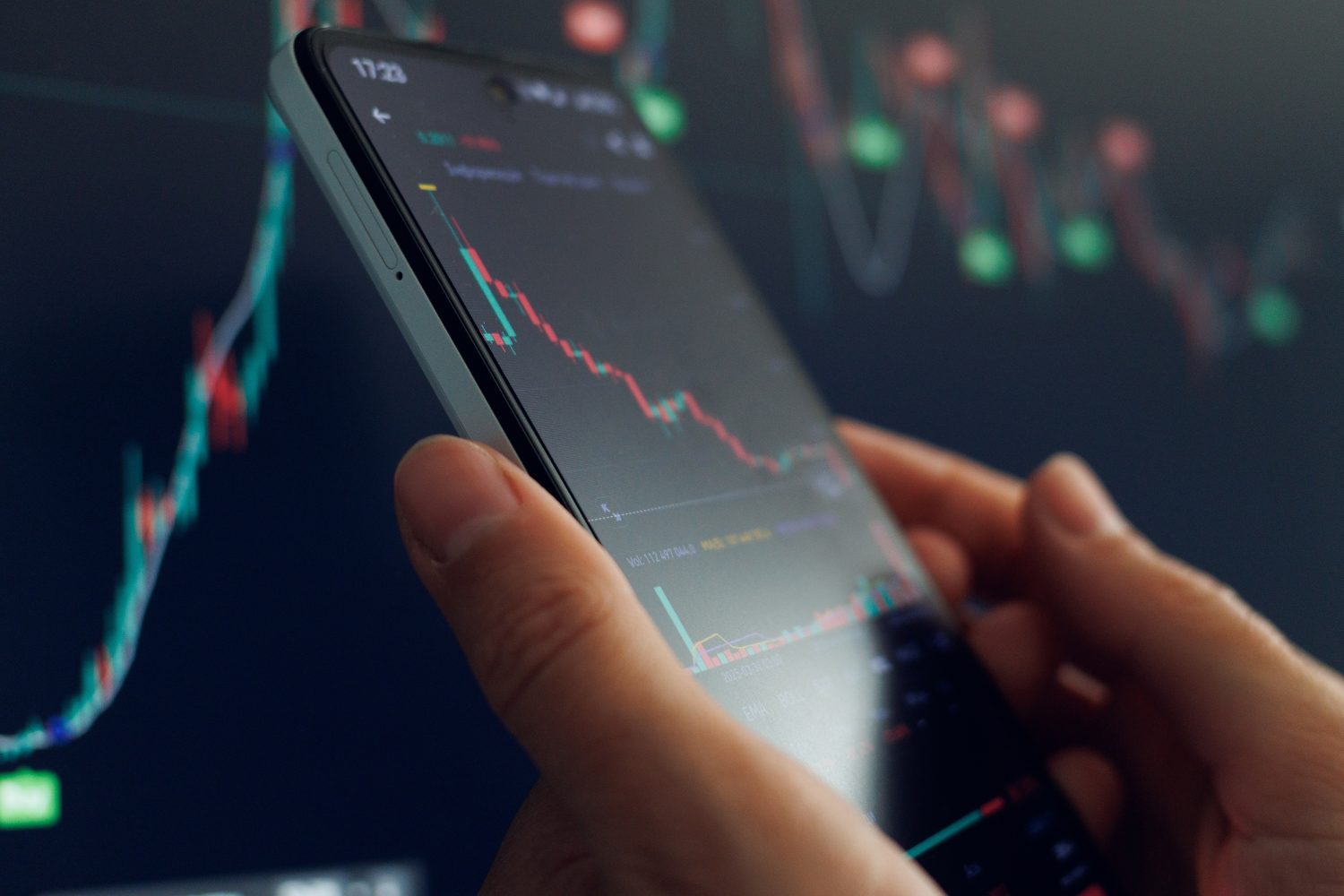 Trader utilizes smartphone to examine fluctuating stock market graphs and data trends during trading hours.