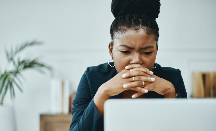 A person looking at laptop with their hands over their mouth, concerned. 